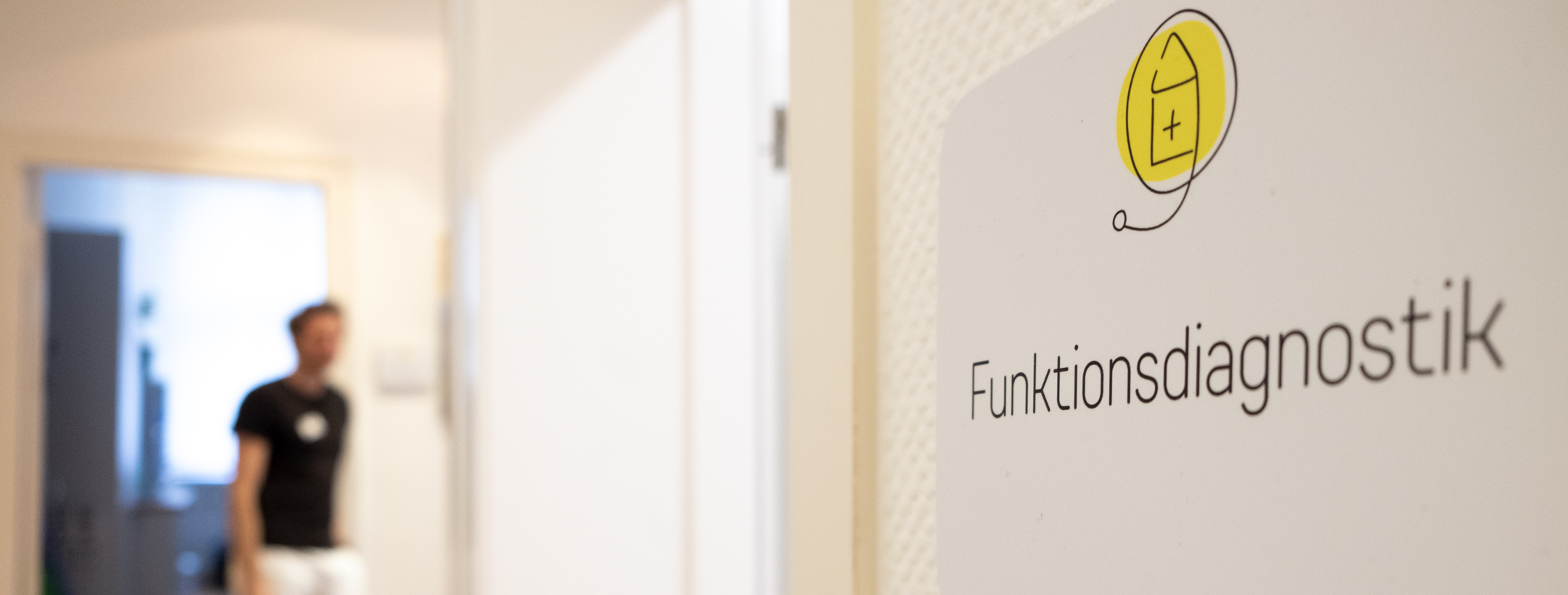 Türschild mit Aufschrift "Funktionsdiagnostik" und Arzt unscharf im Hintergrund.