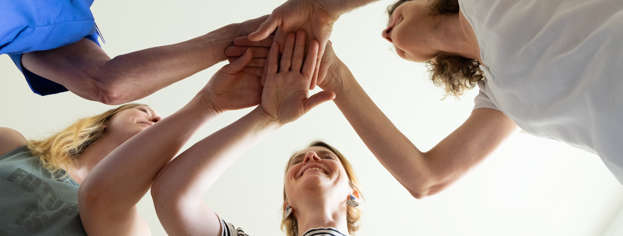 Hände der Teammitglieder übereinandergelegt und von unten fotografiert