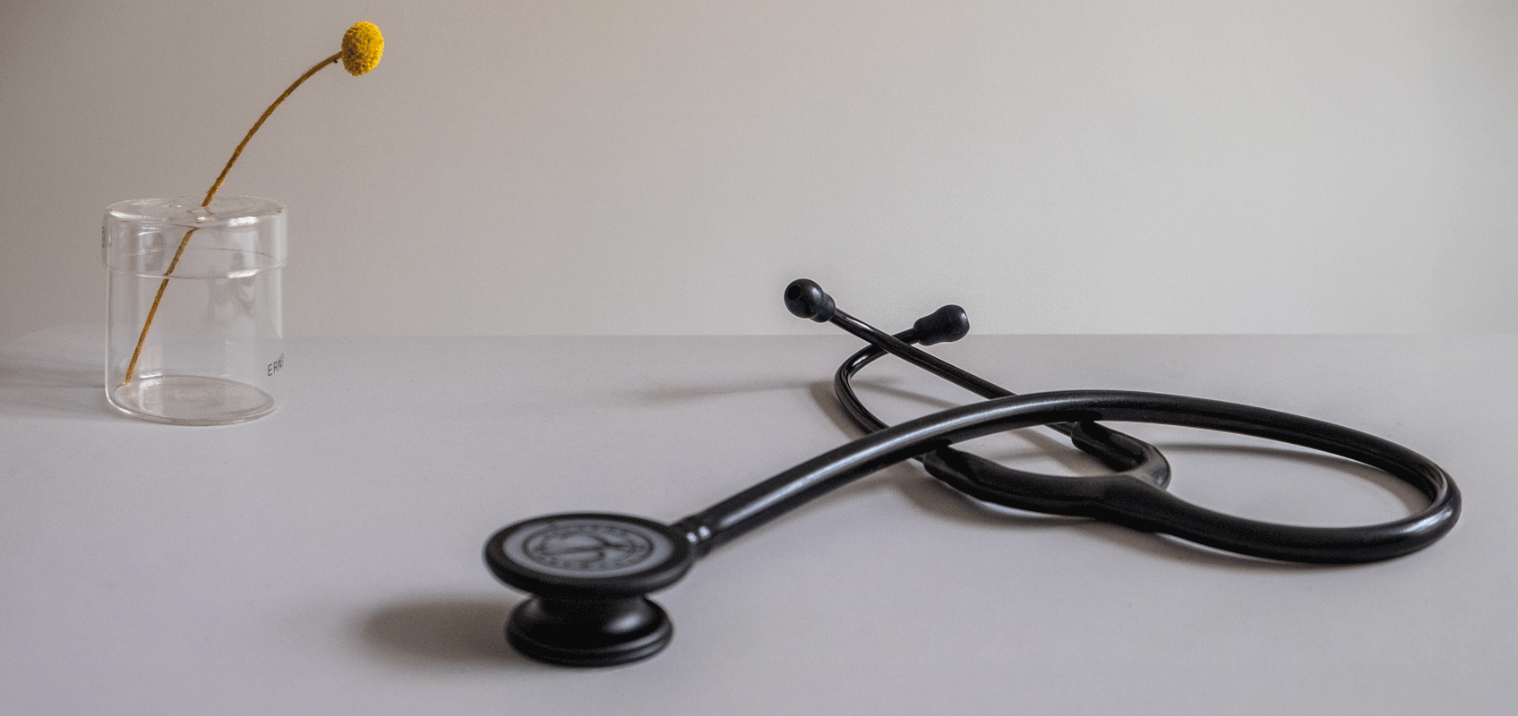 Foto eines Stethoskops neben einer Blume in einer transparenten Vase