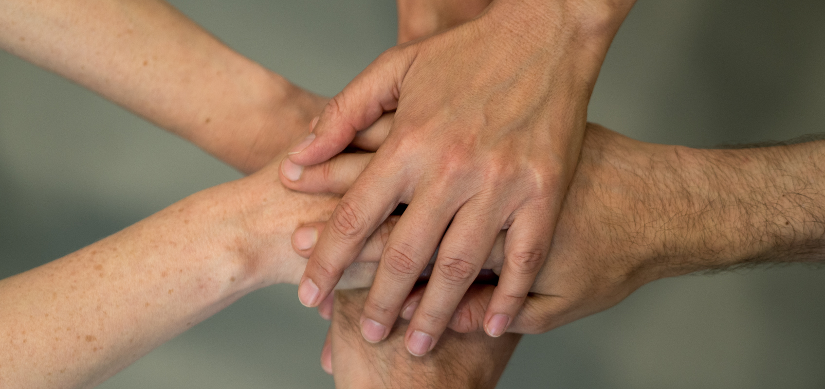 Foto von 6 übereinanderliegenden flachen Händen, von oben aufgenommen