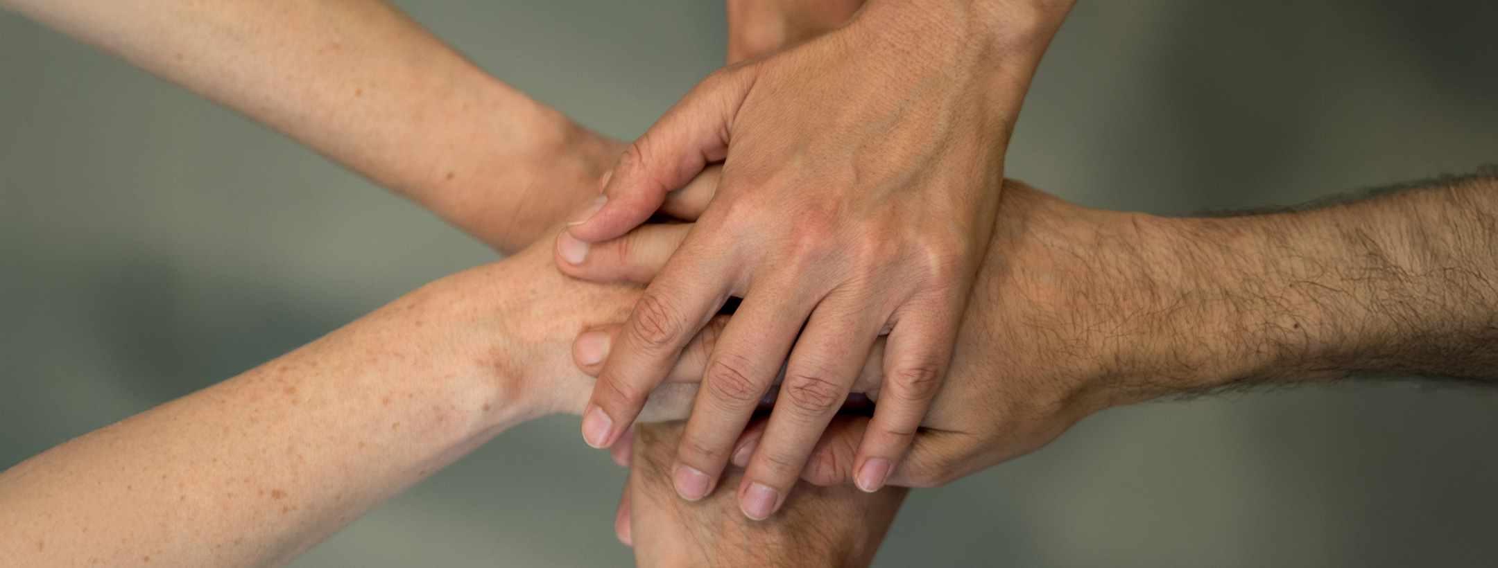 Foto von 6 übereinanderliegenden flachen Händen, von oben aufgenommen